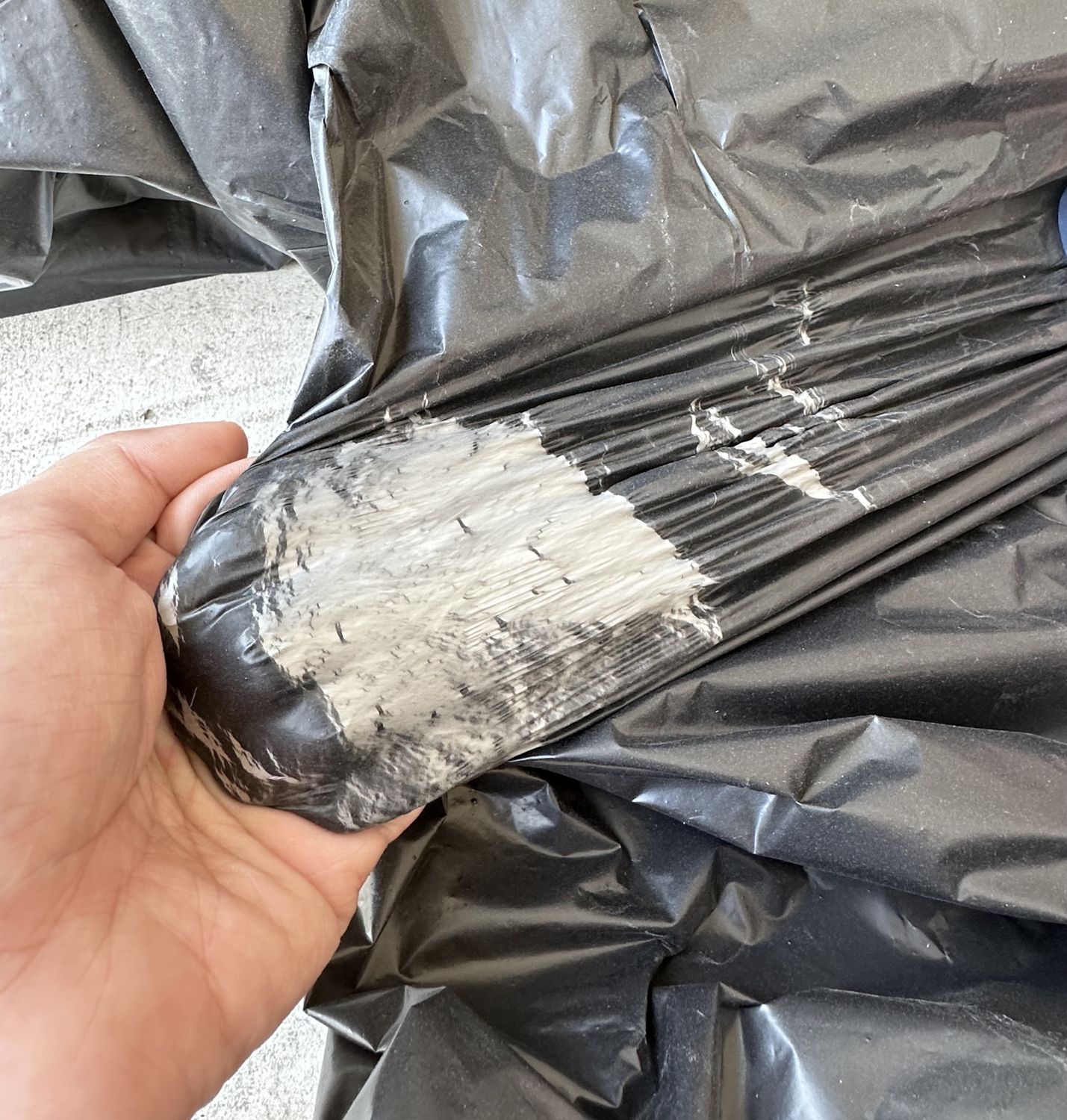 Black garbage bag film stretched by hand, turning white under strain without tearing